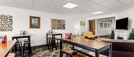 A modern office space with a long wooden table, multiple chairs, a sofa, and a television.