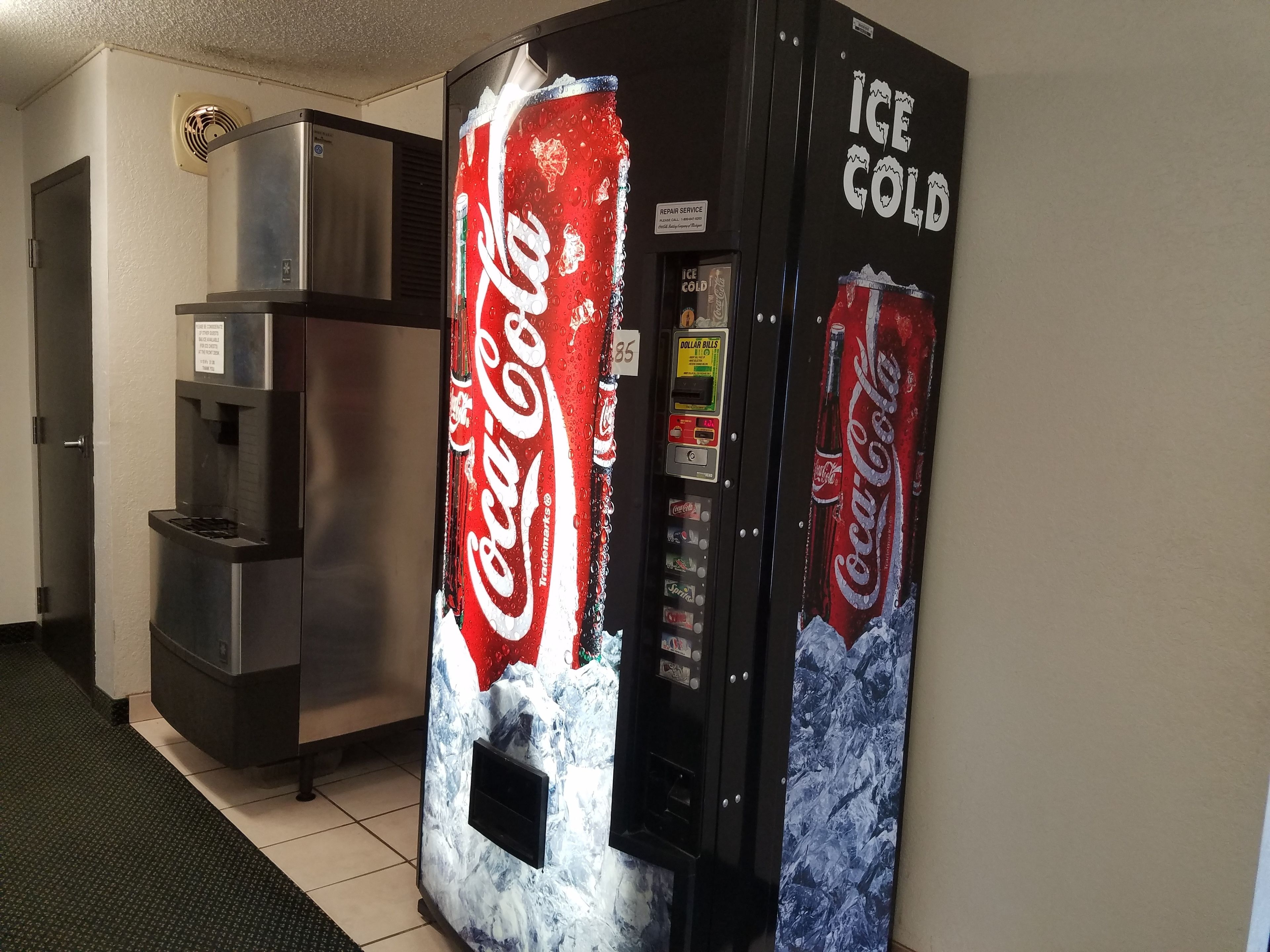 A Coca-Cola vending machine with a large red and white logo, a water dispenser, and a sign for ice service.