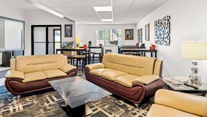 A modern hotel lobby with leather sofas, a coffee table, and a dining area with chairs and tables. - Americas Best Value Inn Tahquamenon Country (Newberry)