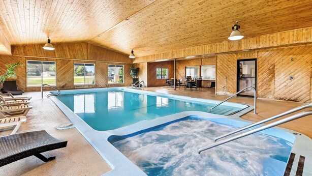 An indoor swimming pool with wooden walls and ceiling, lounge chairs, and a hot tub. - Americas Best Value Inn Tahquamenon Country (Newberry)