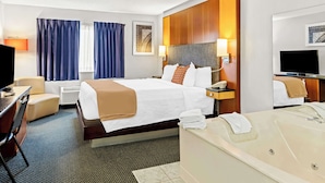 A hotel room with a large bed, a desk with a chair, a desk lamp, a television, a bathroom with a bathtub, and a window with curtains. - Americas Best Value Inn Tahquamenon Country (Newberry)