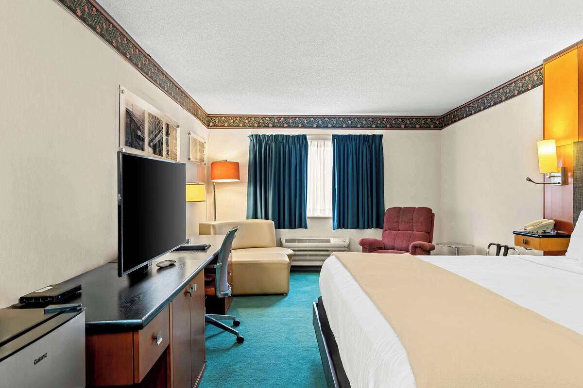 A hotel room with a bed, desk, chair, television, and a window with curtains.