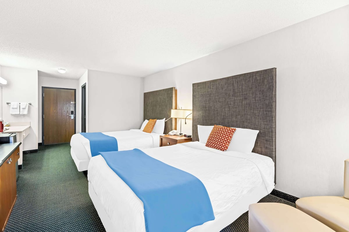A hotel room with two beds, a desk, a chair, and a nightstand with a lamp.