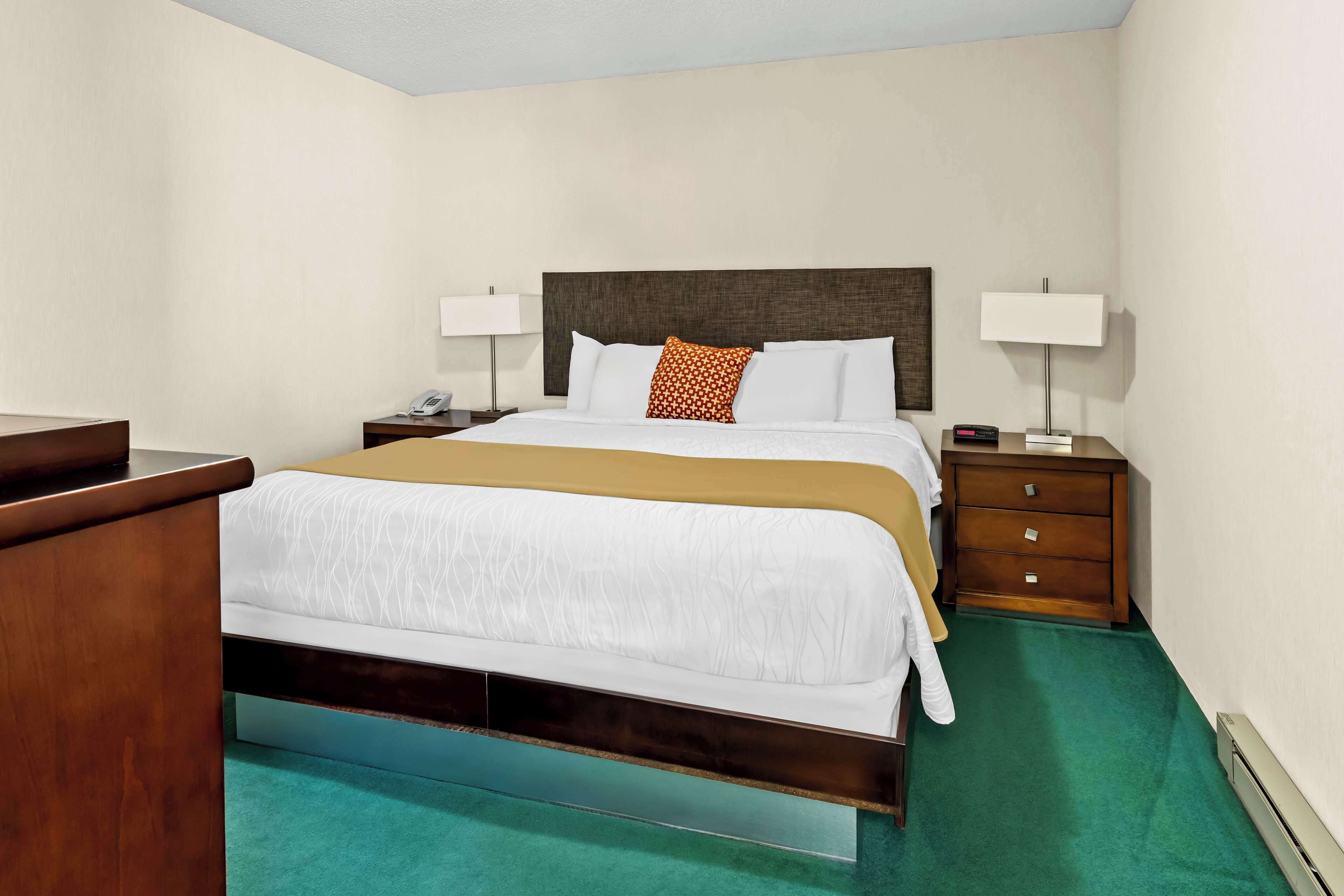 Une chambre d’hôtel avec un lit, des tables de chevet, des lampes et un bureau.