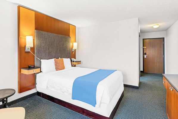 A hotel room with a large bed, bedside lamps, a nightstand, a desk, and a wardrobe. - Americas Best Value Inn Tahquamenon Country (Newberry)