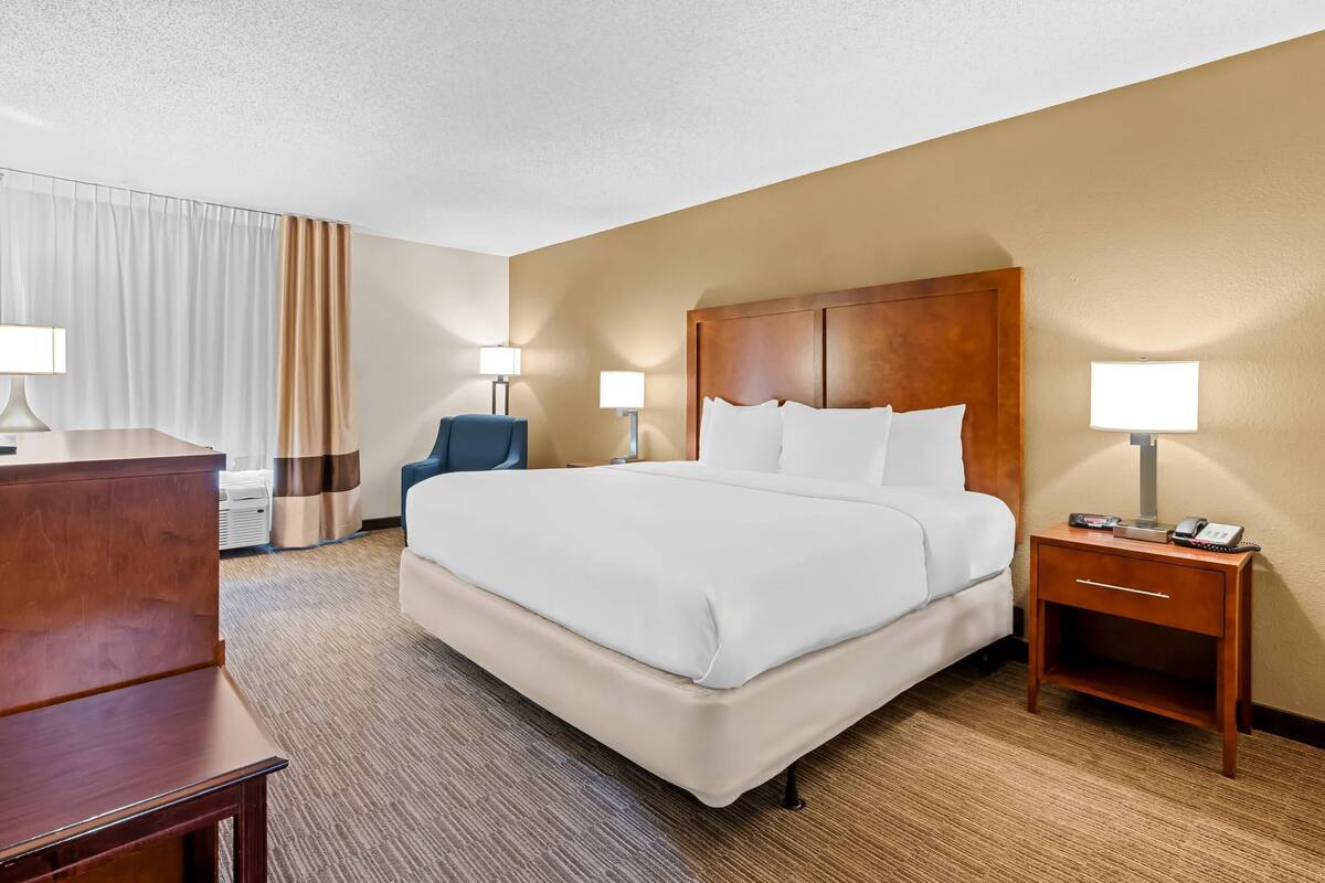 A hotel room with a large bed, bedside lamps, a desk, and a chair.