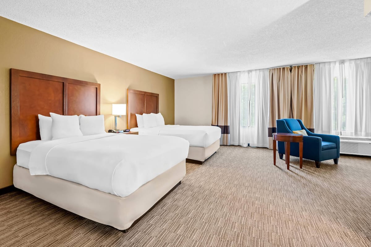 A hotel room with two beds, a desk, a chair, and a large window with curtains.