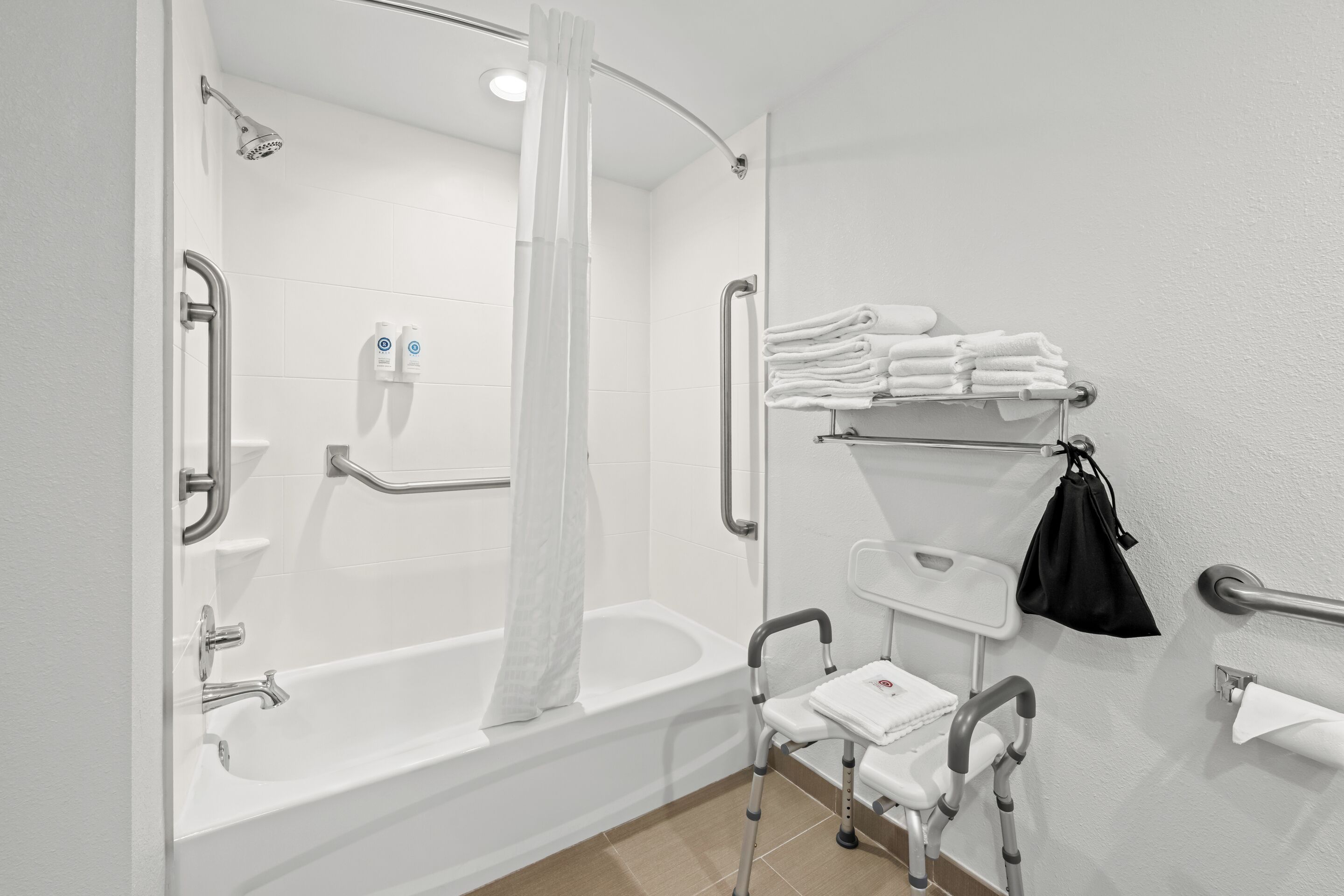 A modern bathroom with a walk-in shower, grab bars, a wheelchair-accessible bench, and neatly stacked towels.