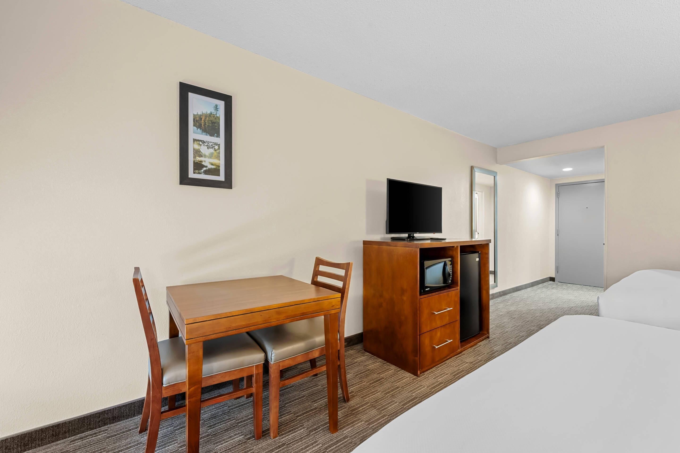 Quarto de hotel com escrivaninha de madeira, televisão sobre um móvel, cama e quadro na parede.