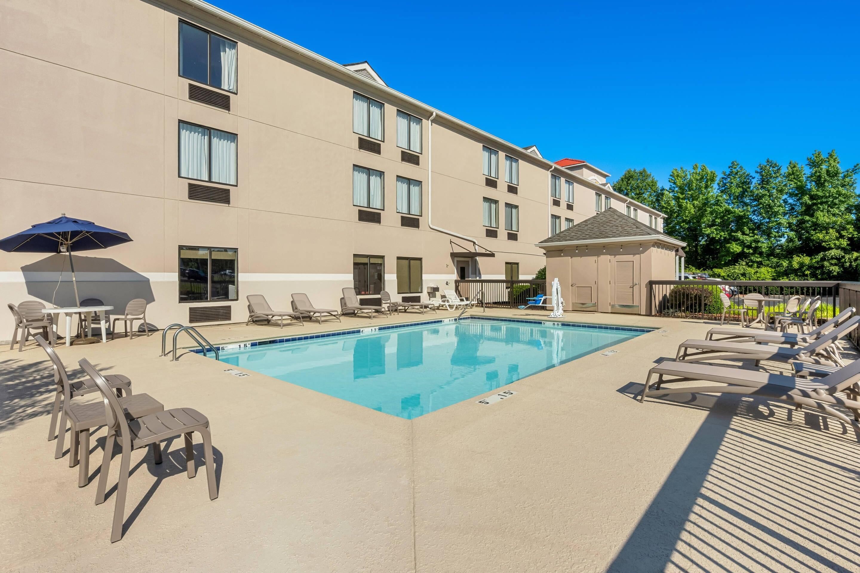 A swimming pool with lounge chairs and umbrellas, surrounded by a building with multiple windows and a covered area.