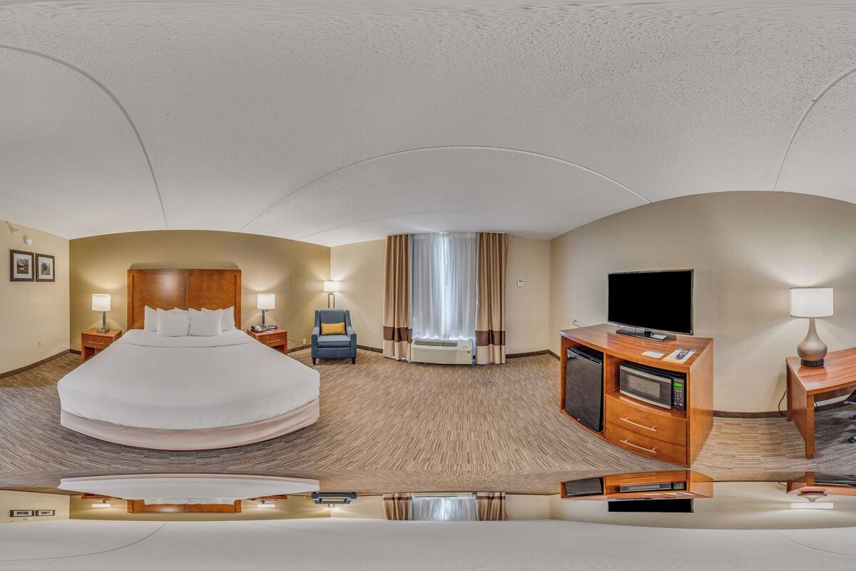 A hotel room with a large bed, a desk with a computer, a TV, and a microwave.
