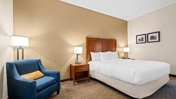 A hotel room with a large bed, a blue armchair, two bedside tables with lamps, and two framed pictures on the wall.