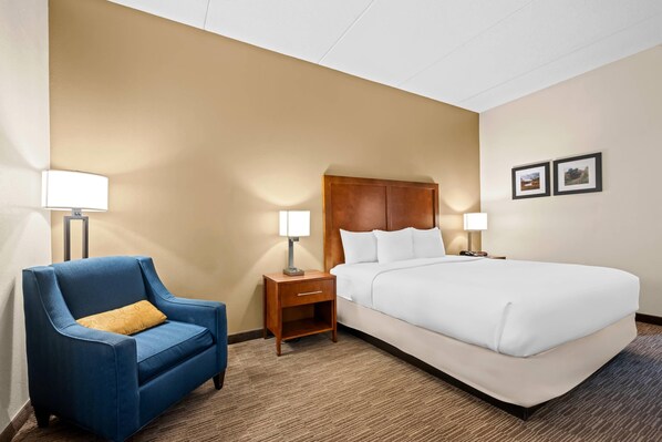 A hotel room with a large bed, a blue armchair, two bedside tables with lamps, and two framed pictures on the wall. - Comfort Inn & Suites Oxford South (Oxford)