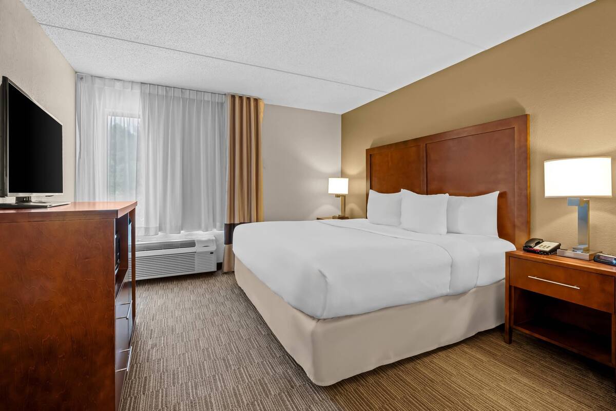 A hotel room with a large bed, a desk with a television, a bedside lamp, and a phone on the nightstand.