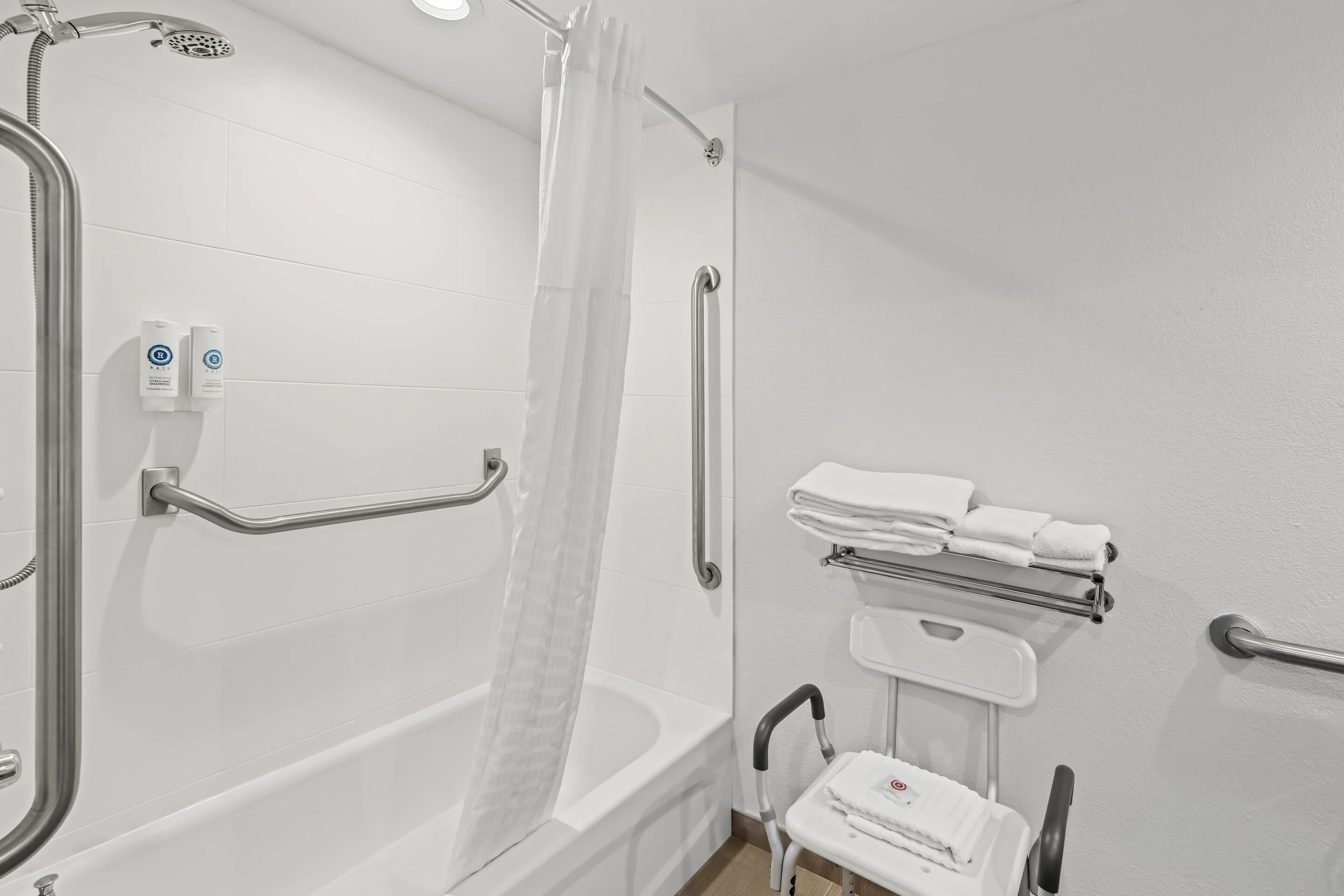 Une salle de bain équipée d’une douche, de barres d’appui, d’un porte-serviettes et d’un banc accessible aux personnes en fauteuil roulant.