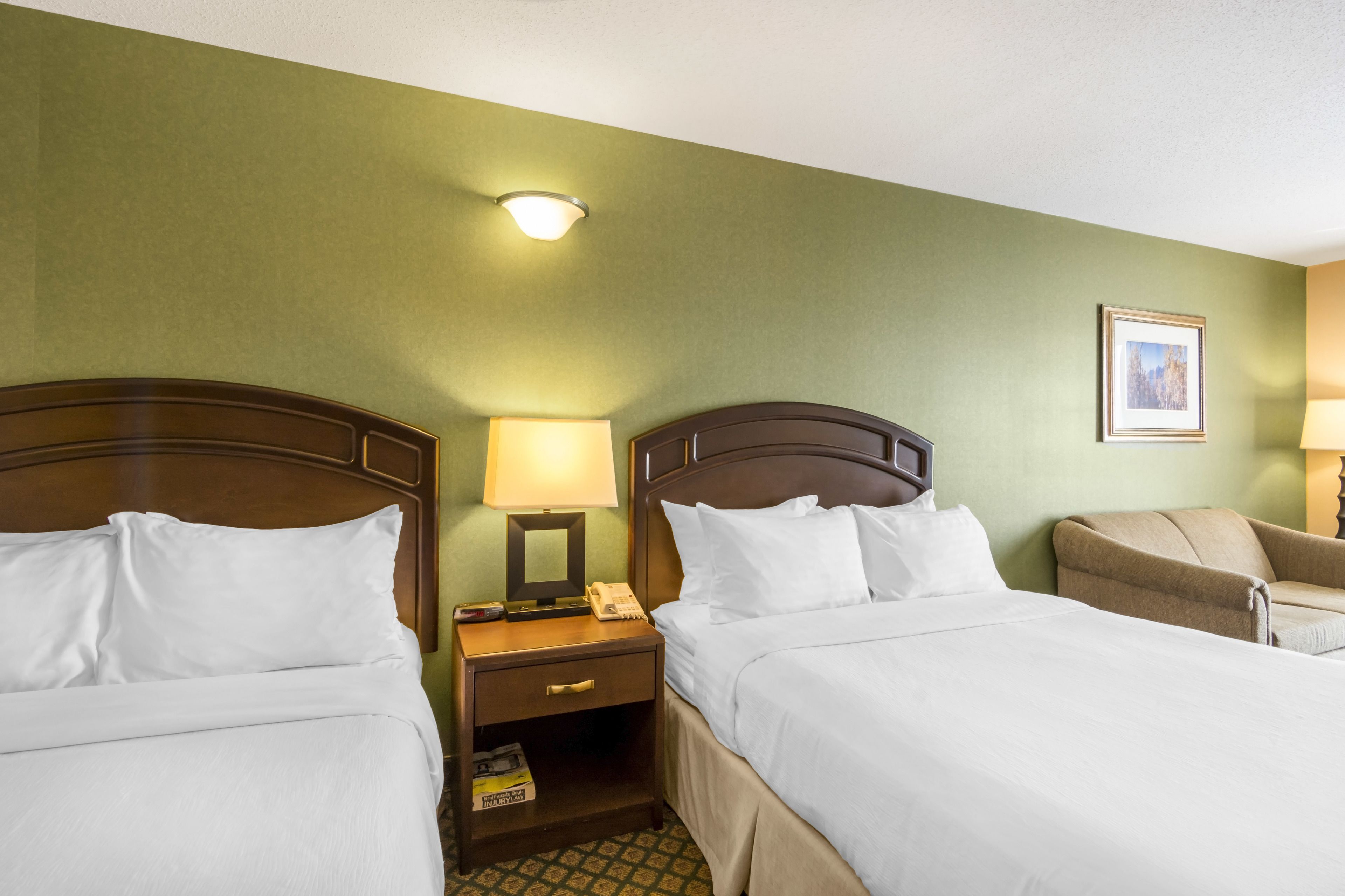 Une chambre d’hôtel avec deux lits, une table de chevet avec une lampe, une chaise et un tableau encadré au mur.