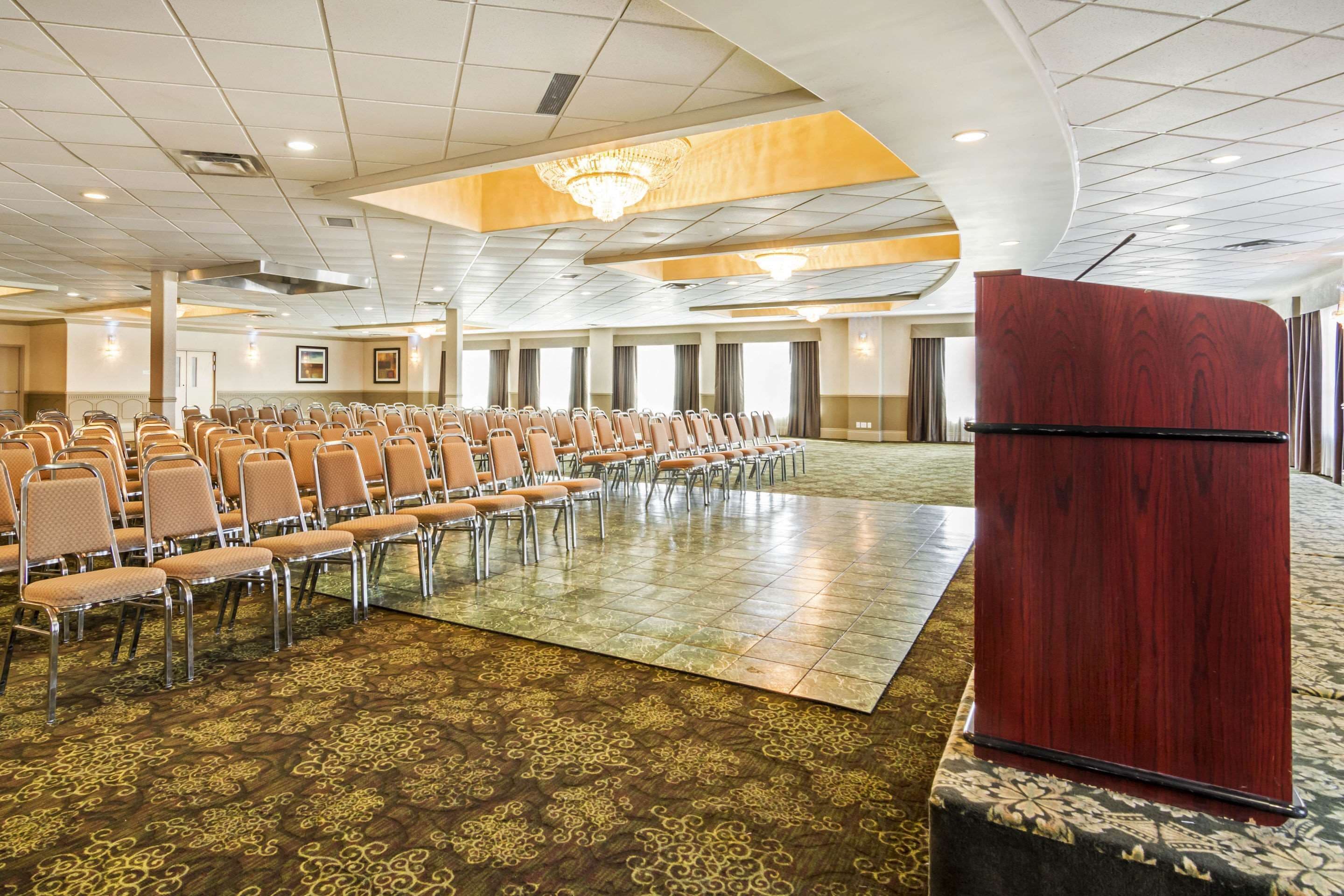 A conference room with rows of chairs, a podium, and a patterned carpet.