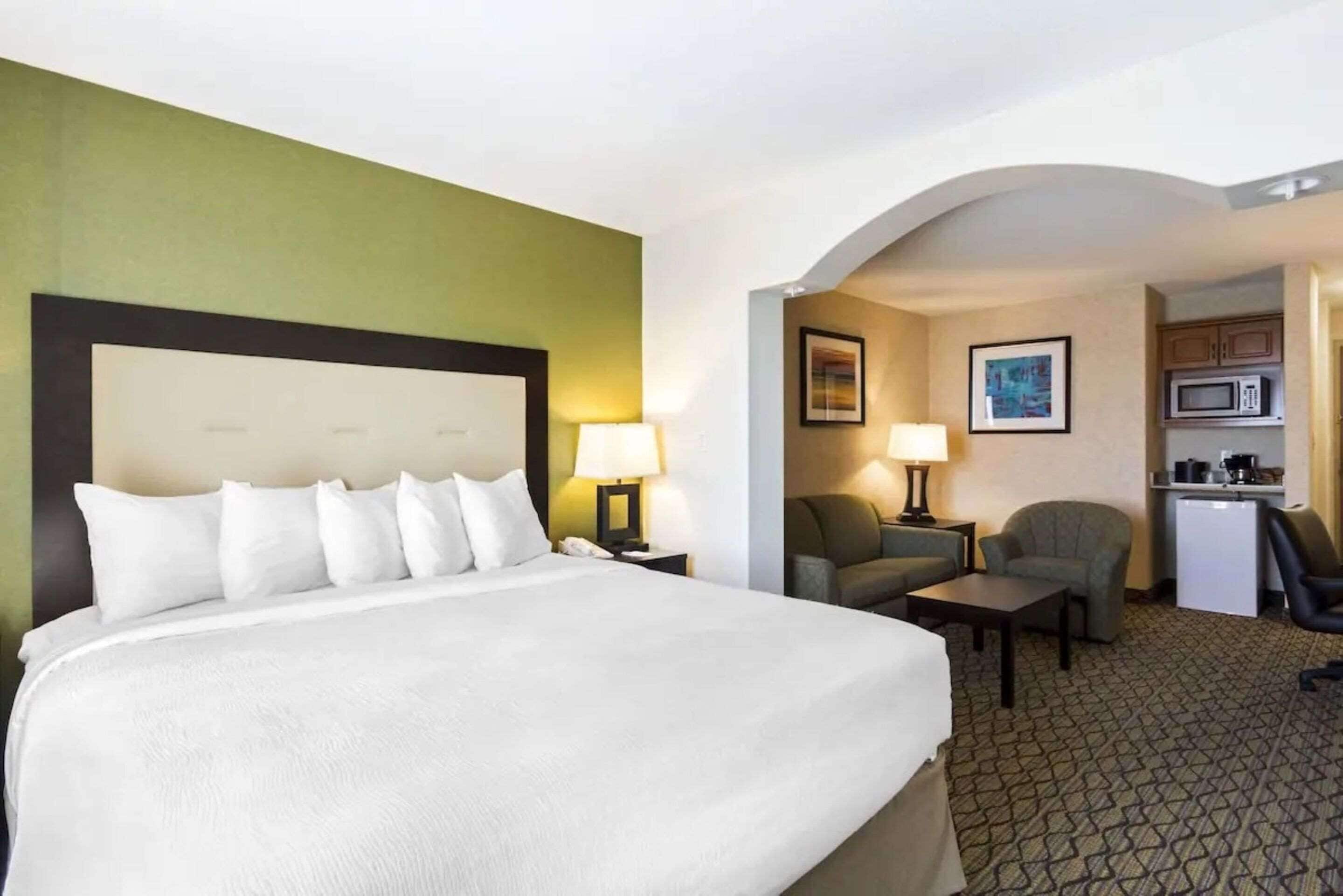 A hotel room with a large bed, a desk, a chair, a sofa, a microwave, and a small kitchenette.