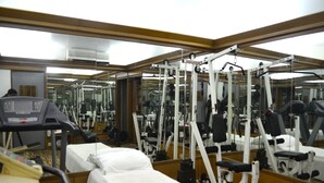 Une salle de sport équipée de machines d’exercice, d’un tapis de course et d’un mur recouvert de miroirs.