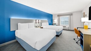Habitació d'hotel amb dos llits, una taula de treball, una cadira, una làmpada i una finestra gran.