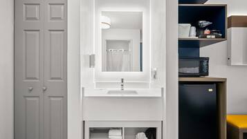 A bathroom with a white sink, mirror, and a black refrigerator.