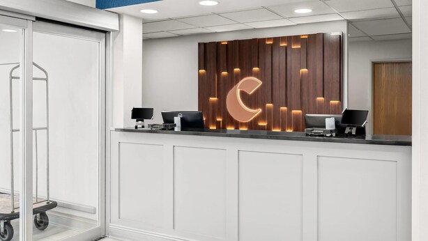Tauleller de recepció de disseny modern, amb un gran logotip il·luminat, dos monitors d'ordinador i un carret.