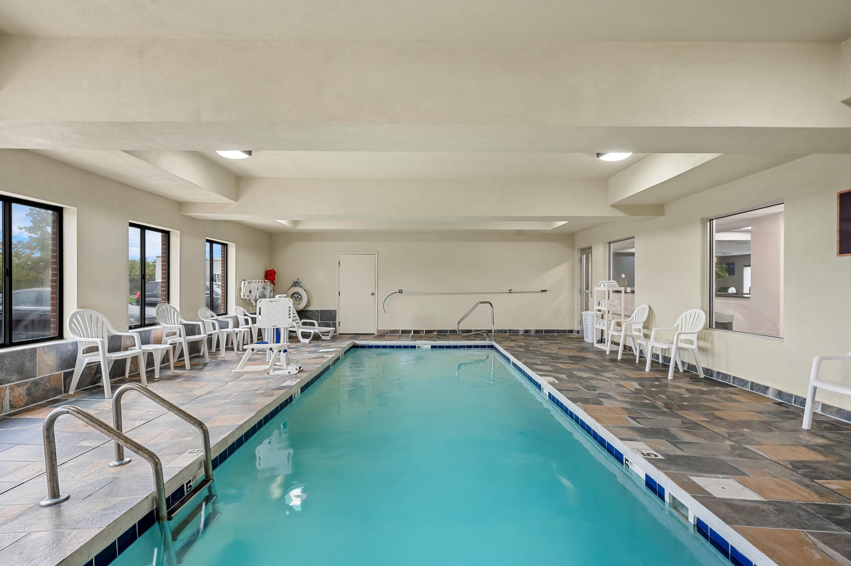 An indoor swimming pool with clear blue water, surrounded by white chairs and a tiled floor.