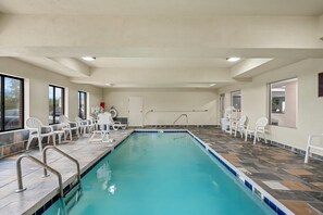 An indoor swimming pool with clear blue water, surrounded by white chairs and a tiled floor.