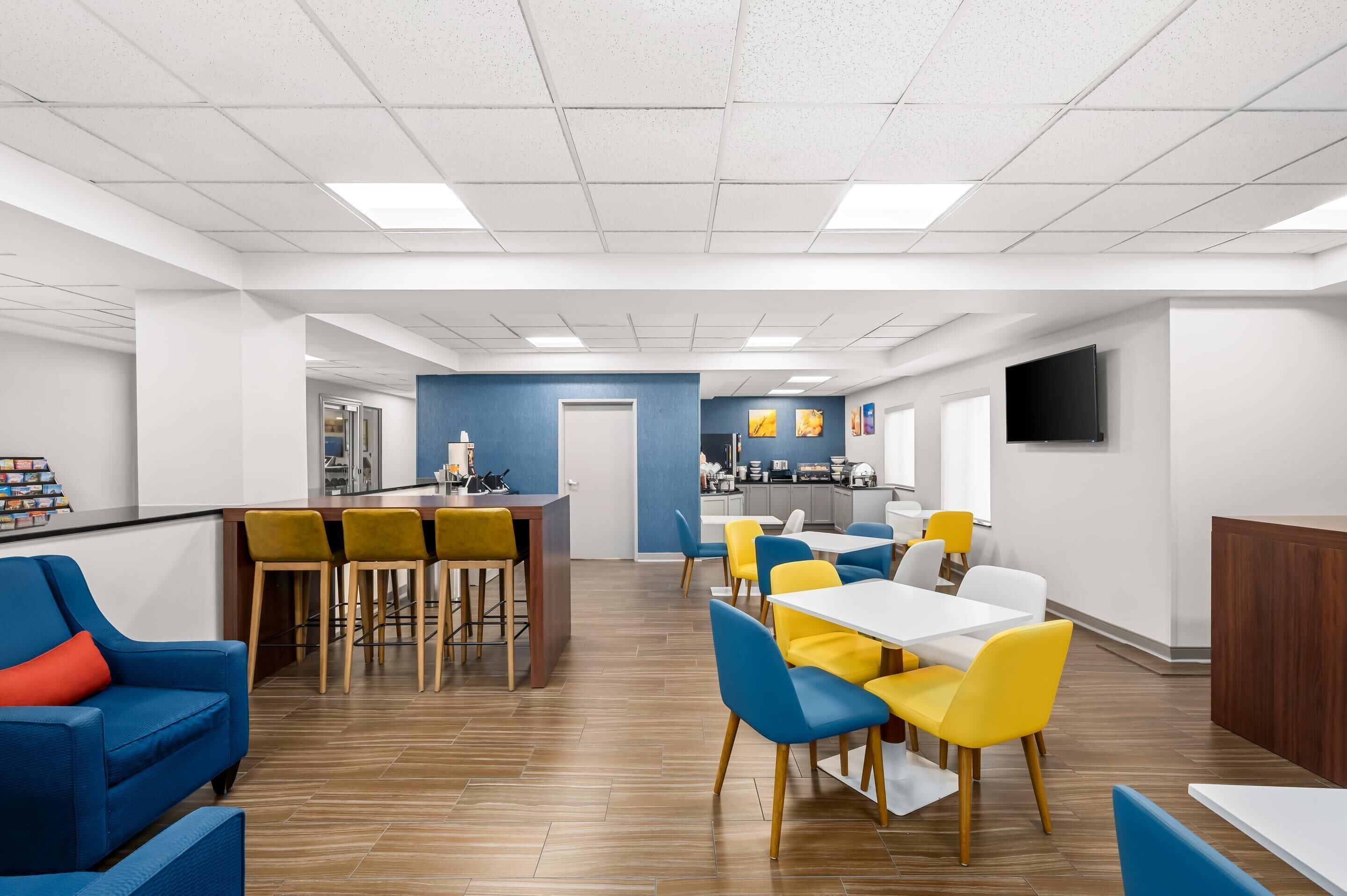 A modern dining area with a bar, yellow and blue chairs, and a kitchen in the background.