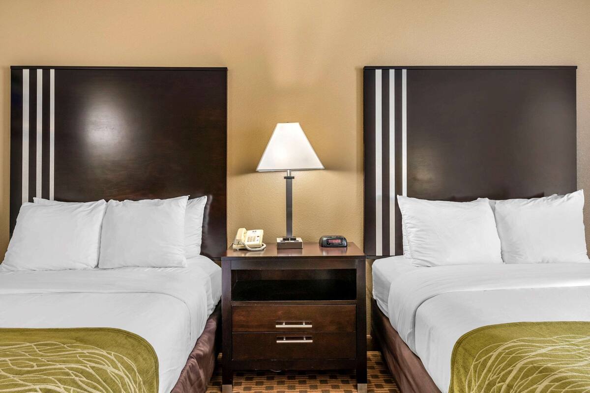 A hotel room with two beds, a nightstand with a lamp, a phone, and a digital clock.