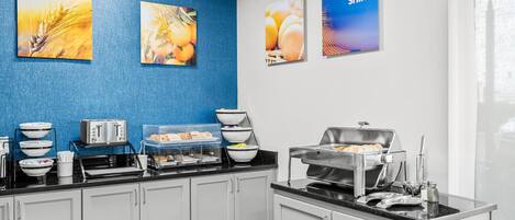 Una barra de desayuno con diferentes alimentos y electrodomésticos, incluyendo un tostador y una máquina para hacer gofres.