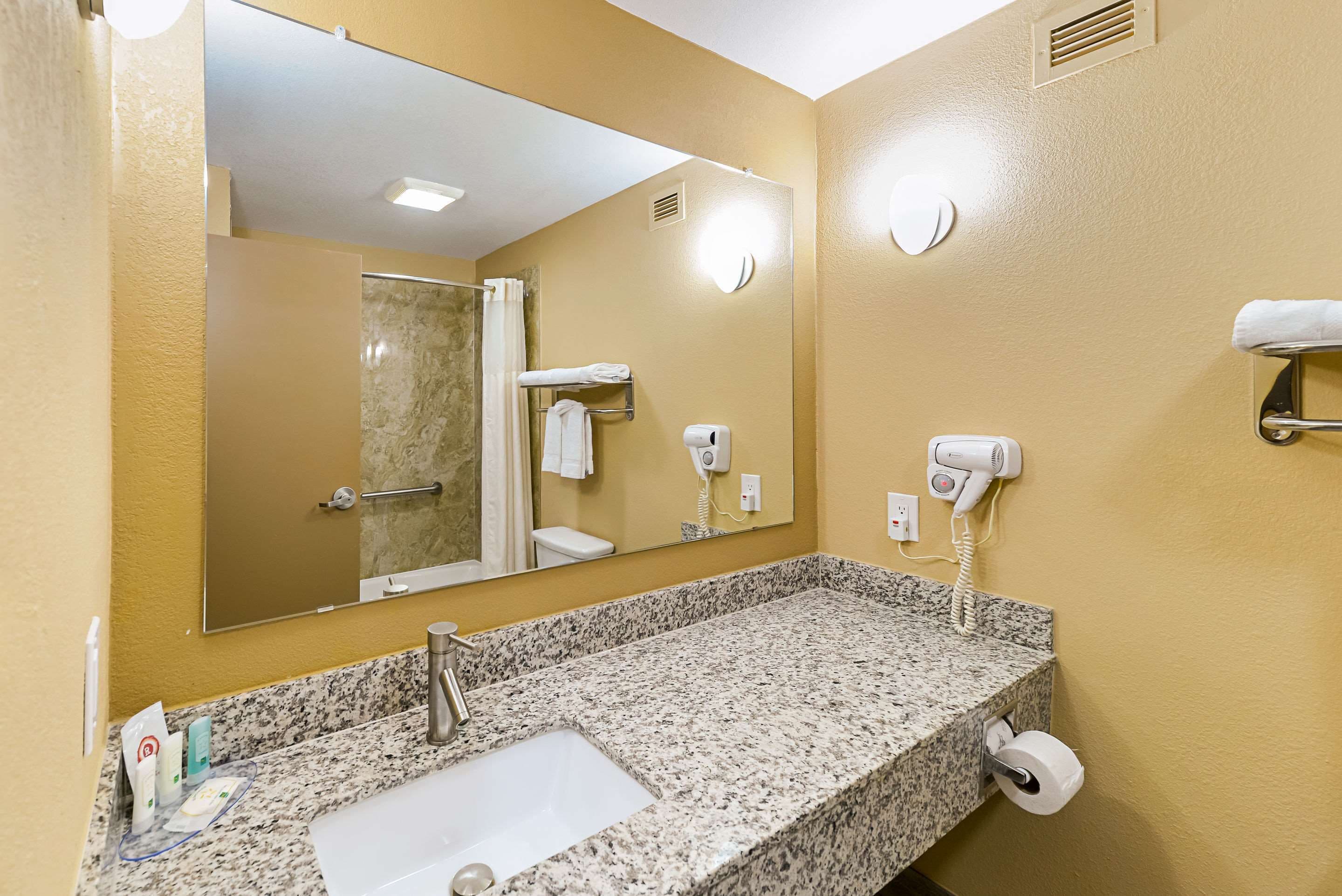 Baño con encimera de granito, lavamanos, espejo, toallero y secador de pelo.