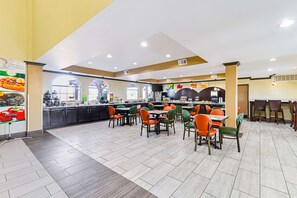 A spacious restaurant with multiple dining tables and chairs, a kitchen area, and large windows.