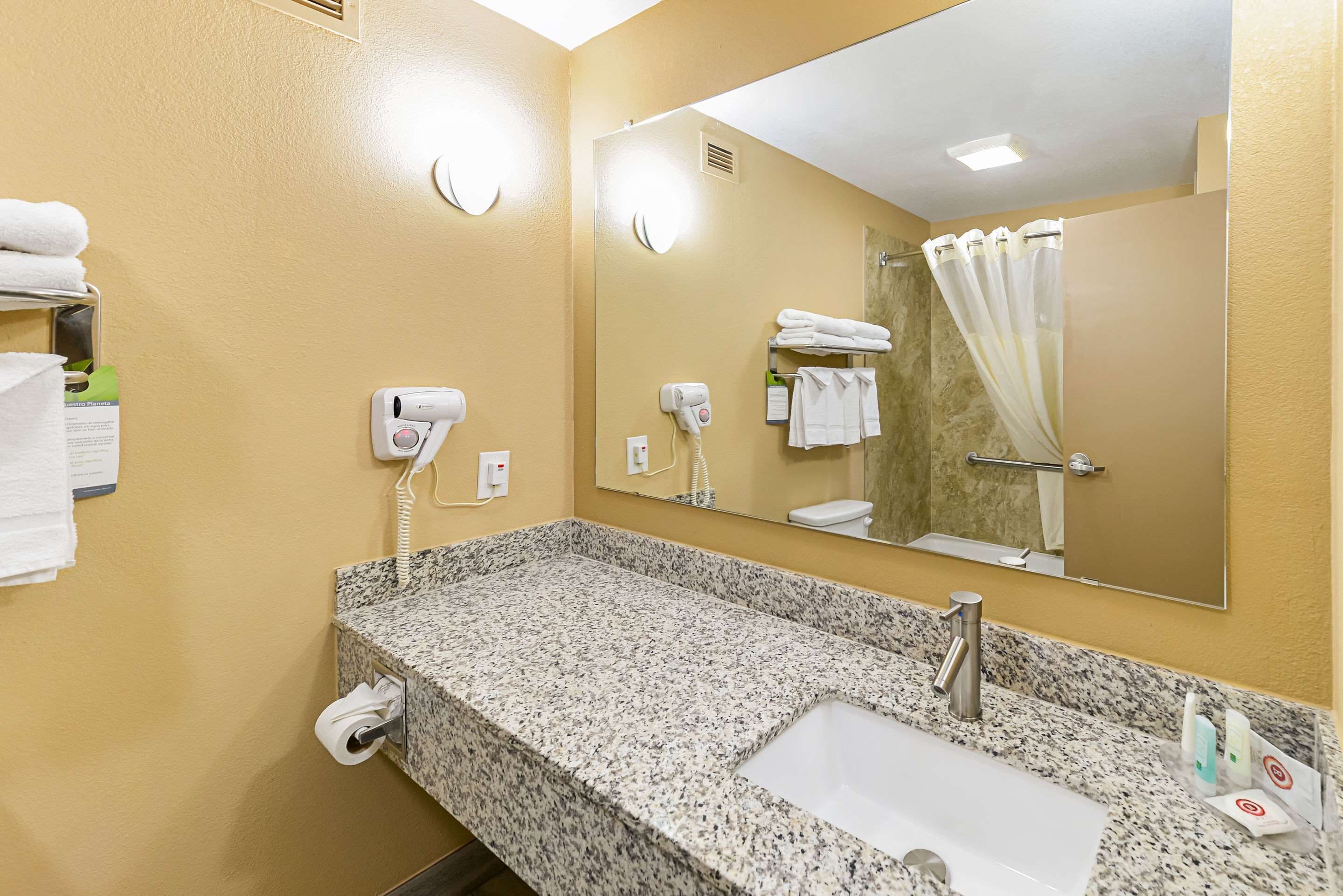 Une salle de bain d’hôtel avec un lavabo doté d’un plan de travail en granit, un miroir, un porte-serviettes et un rideau de douche.