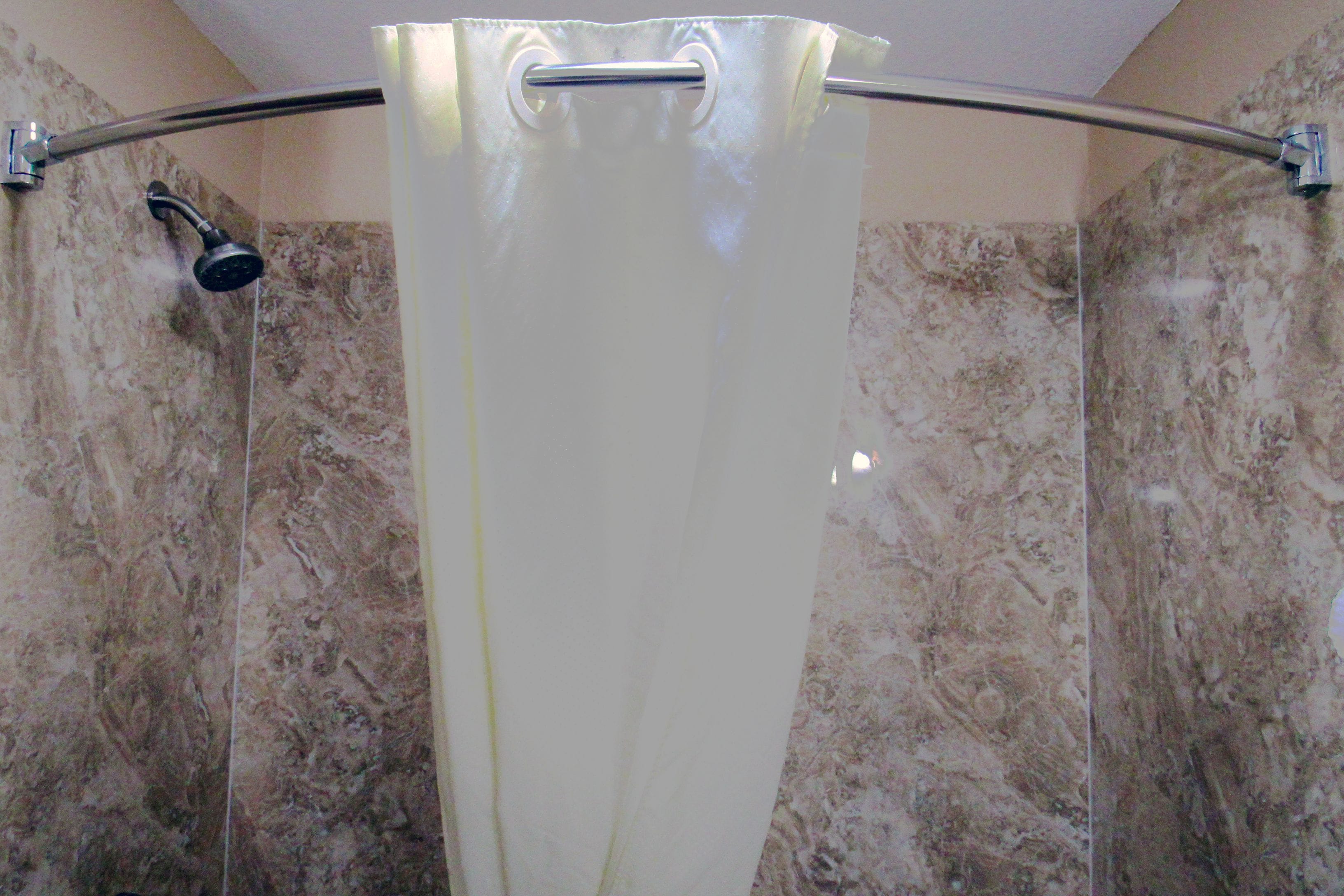 Une tringle à rideau de douche avec un rideau de douche dans une salle de bain aux murs en marbre.