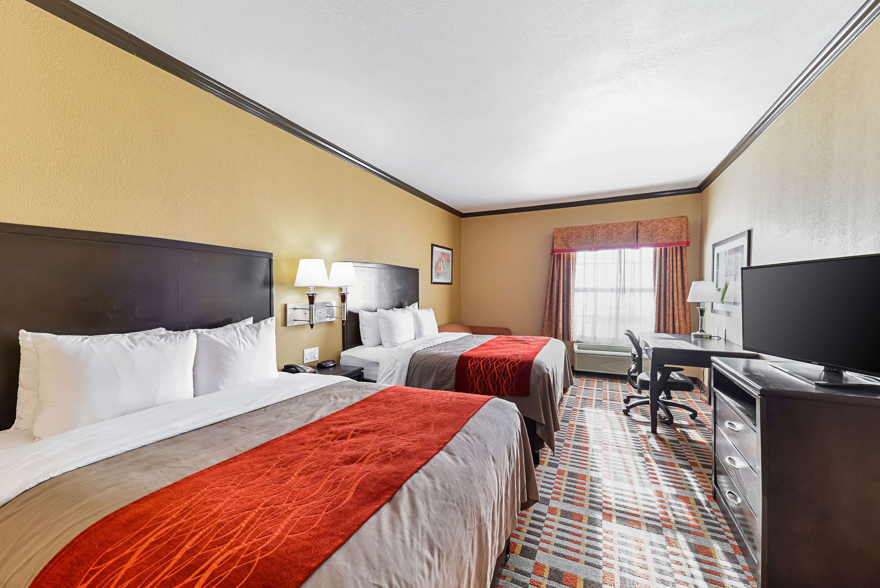A hotel room with two beds, a desk, a chair, a television, and a window with curtains.