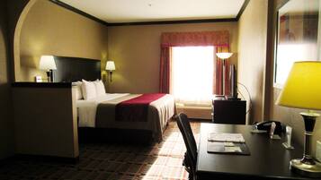 A hotel room with a bed, desk, chair, lamps, and a window with curtains.