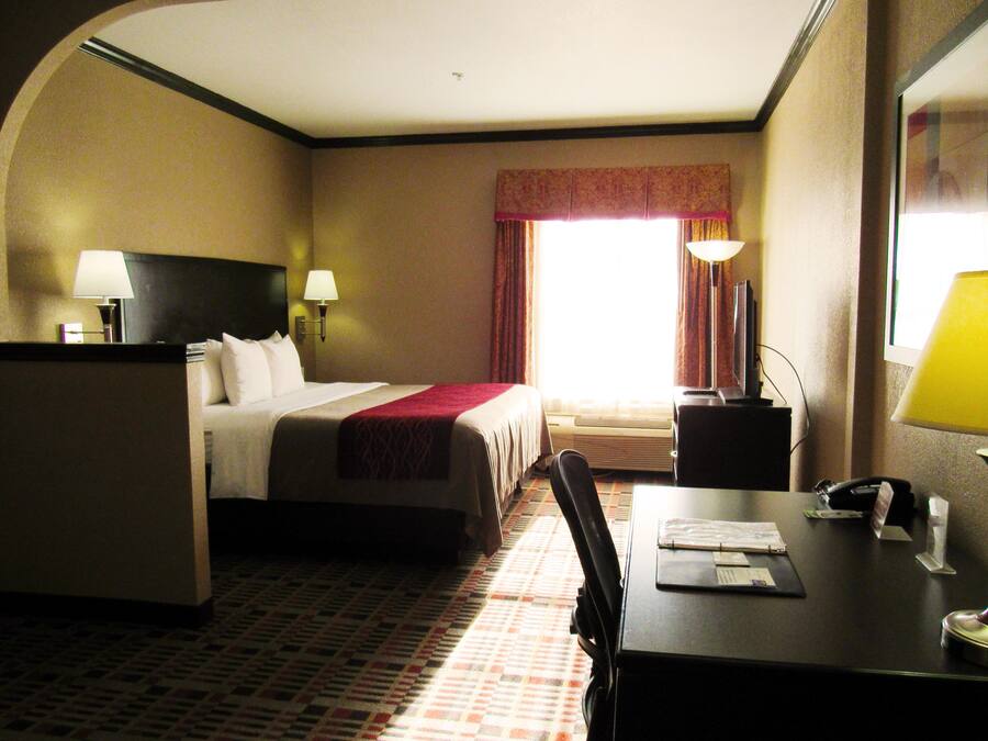 A hotel room with a bed, desk, chair, lamps, and a window with curtains.