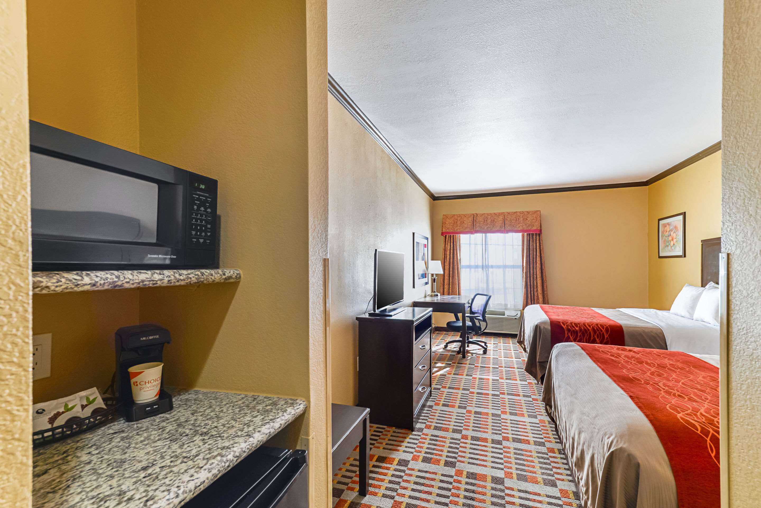 Een hotelkamer met een magnetron, koffiezetapparaat, bureau, computer en twee bedden.