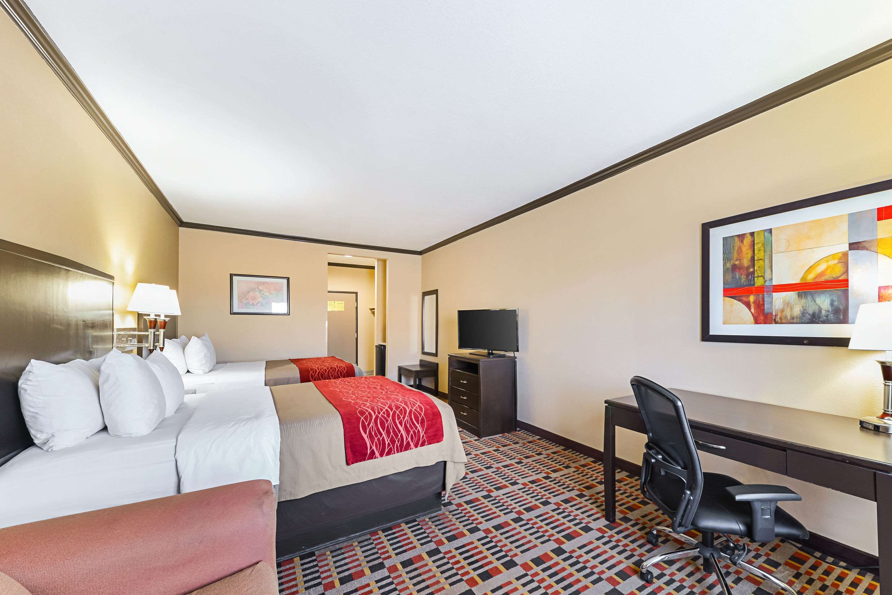 A hotel room with a large bed, a desk, a chair, a TV, and a painting on the wall.