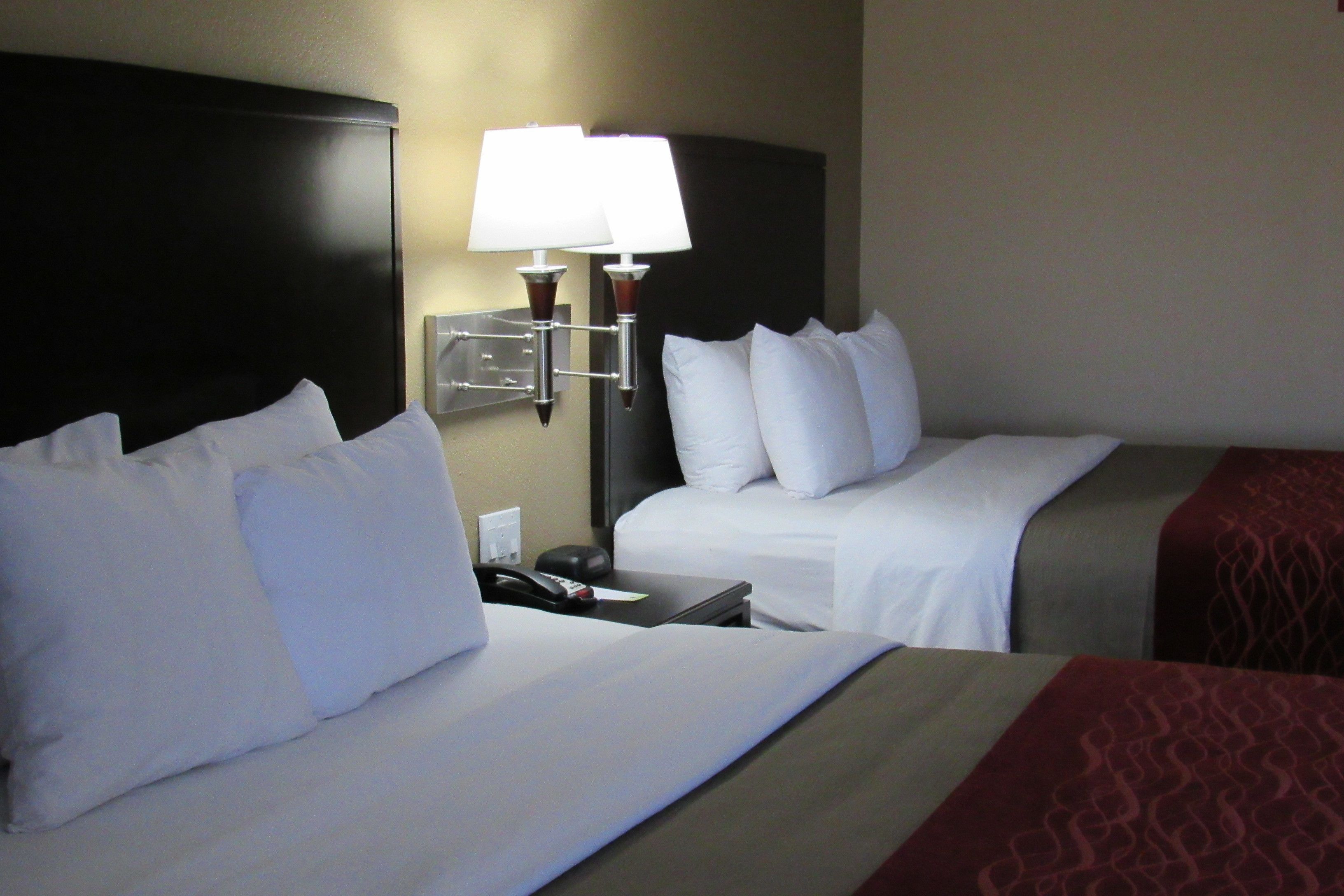 Quarto de hotel com duas camas, mesa de cabeceira com abajur e telefone fixado na parede.