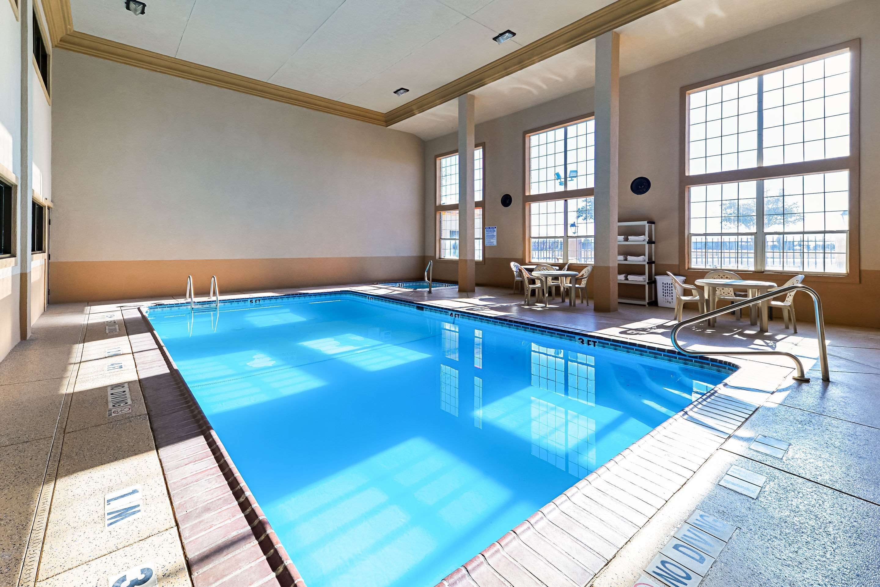 Una amplia piscina interior con agua cristalina, rodeada por un solárium con baldosas y grandes ventanales.