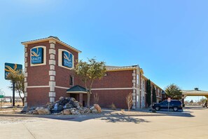 A brick building with "Quality Inn & Suites" signage, a parking area, and a clear blue sky.
