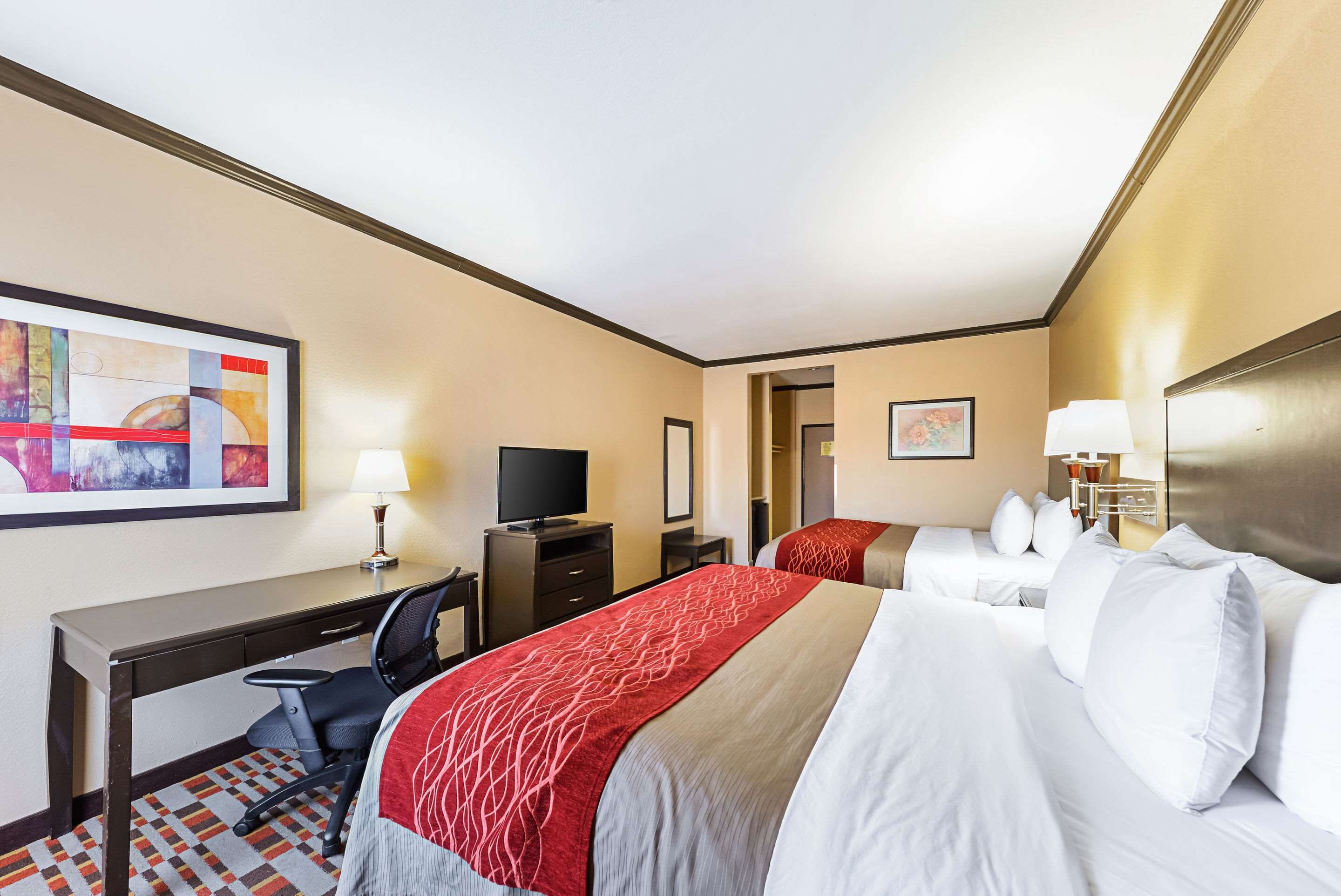 Een hotelkamer met een bureau, twee bedden, een televisietoestel en kunstwerken aan de wanden.