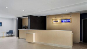 A hotel reception desk with a 'Welcome City Express by Marriott' sign, a blue chair, and a small table.