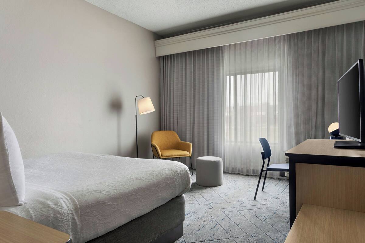 Una habitación de hotel con cama, escritorio, silla, lámpara y televisión.