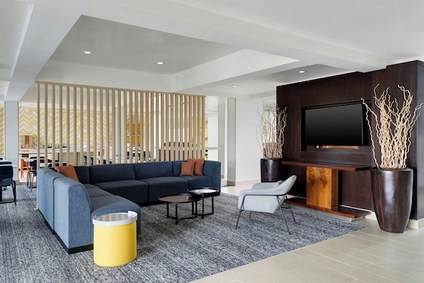 A modern living room with a sectional sofa, a flat-screen TV, a coffee table, and a potted plant.
