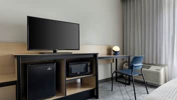 A hotel room with a TV, a small fridge, a microwave, a desk, a chair, and a bed.
