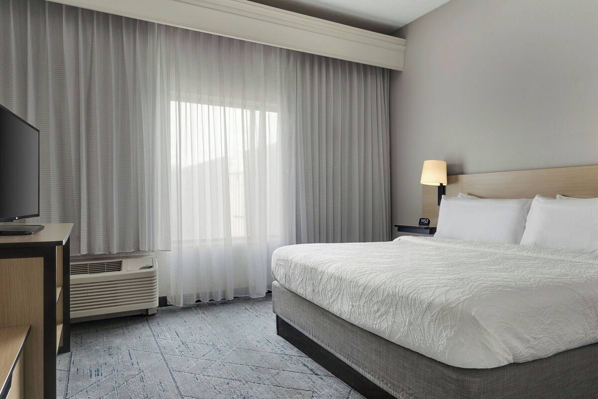Una habitación de hotel con una cama, un televisor, una lámpara y una ventana con cortinas.
