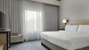 A hotel room with a bed, a TV, a lamp, and a window with curtains.